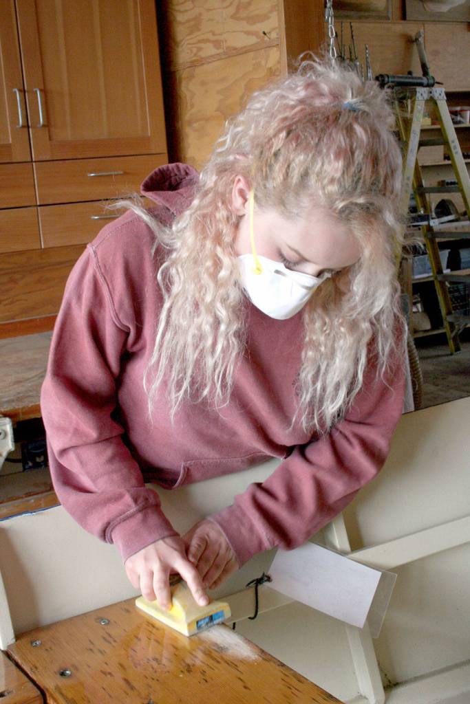 Briana Martin, part of the Real World Readiness program at the Northwest Maritime Center, uses sandpaper on a wooden boat Wednesday. (Brian McLean/Peninsula Daily News)
