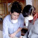 Instructor Ariela Marshall teaches Kira McDowell how to use sandpaper with the grain as they work on a wooden boat Wednesday at the Northwest Maritime Center. (Brian McLean/Peninsula Daily News)