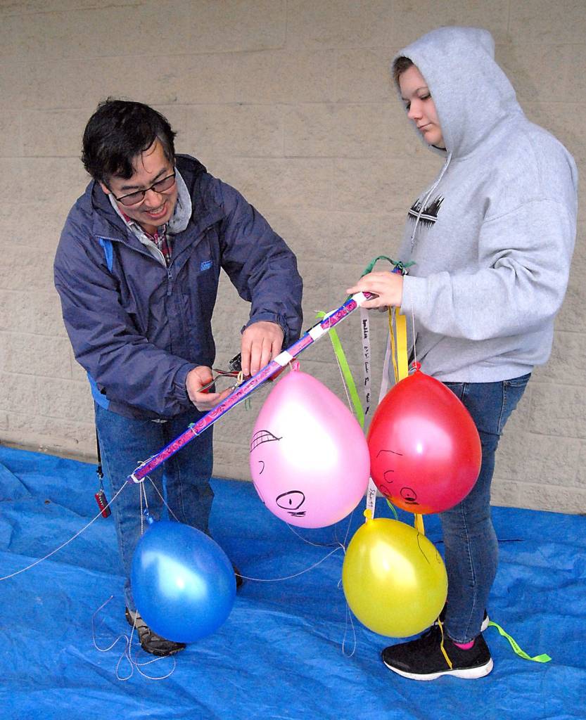 Robert Winglee, director of the Washington NASA Grant Consortium at the University of Washington, left, makes adjustments to a camera mounted on a framework holding balloons standing in as astronauts, ribbons with the names of students and two packets of seeds to be carried on the balloon. (Keith Thorpe/Peninsula Daily News)
