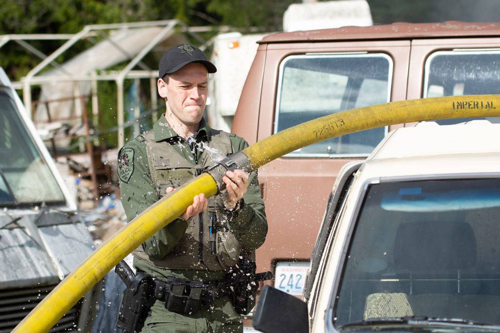 Lower Elwha Klallam Police Officer Dylan Heck lifts a hose over a vehicle as firefighters from Clallam Fire District 2 battle a blaze in the 200 block of Kacee Way on Wednesday afternoon. (Jesse Major/Peninsula Daily News)