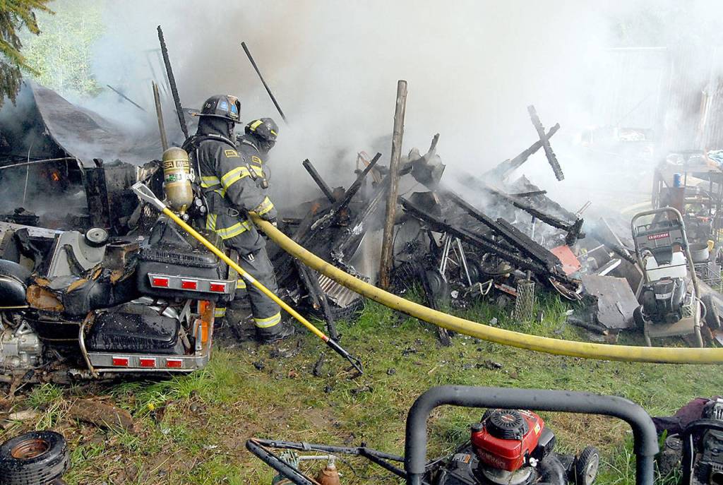 Firefighters from Clallam County Fire District 2 look over the remains of a mobile home that burned in the 200 block of Kacee Way west of Port Angeles on Wednesday. (Keith Thorpe/Peninsula Daily News)