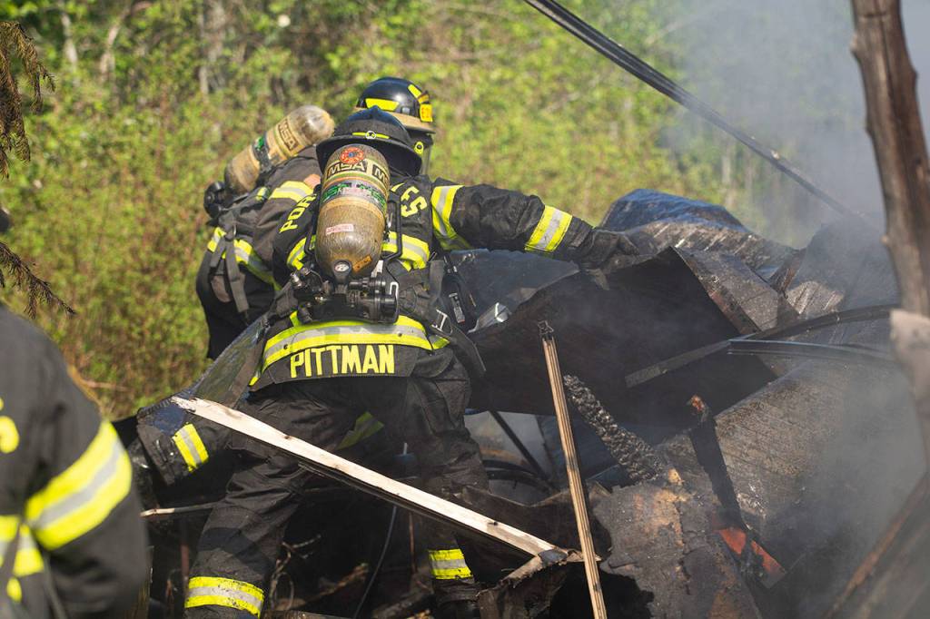 Andrew Pittman, a firefighter with Clallam Fire District 2, shifts through debris at a fire on Kacee Way west of Port Angeles on Wednesday afternoon. (Jesse Major/Peninsula Daily News)