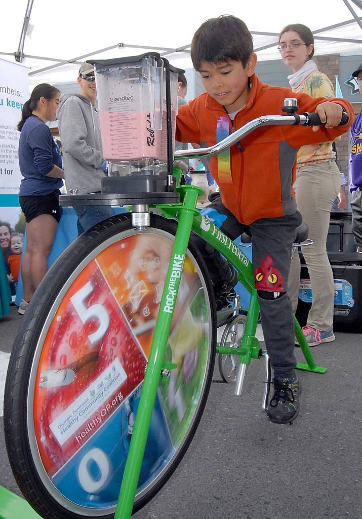 Coleman Keate, 7, of Sequim pedals a stationary bicycle attached to a blender to make a smoothie created with human power at an activity booth set up by Molina Heathcare. (Keith Thorpe/Peninsula Daily News)