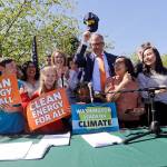 Gov. Jay Inslee, center, pulls off his 100% cap, standing for a goal of 100 percent clean energy, after posing for a photo with supporters after signing climate protection legislation Tuesday in Seattle. (Elaine Thompson/The Associated Press)