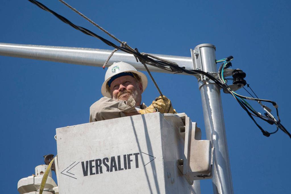 A lineman lifts a line as the Horizon Center passes underneath. (Jesse Major/Peninsula Daily News)