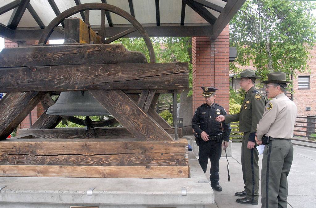 The Liberty Bell at Veterans Park is rung by, from left, Port Angeles Police Chief Brian Smith, U.S. Border Patrol Officer in Charge Corey Lindsay and Clallam County Sheriff Bill Benedict. (Keith Thorpe/Peninsula Daily News)
