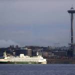 A Washington State ferry heading into Elliott Bay is illuminated by the sun as the city behind remains under clouds in Seattle. (Elaine Thompson/The Associated Press)
