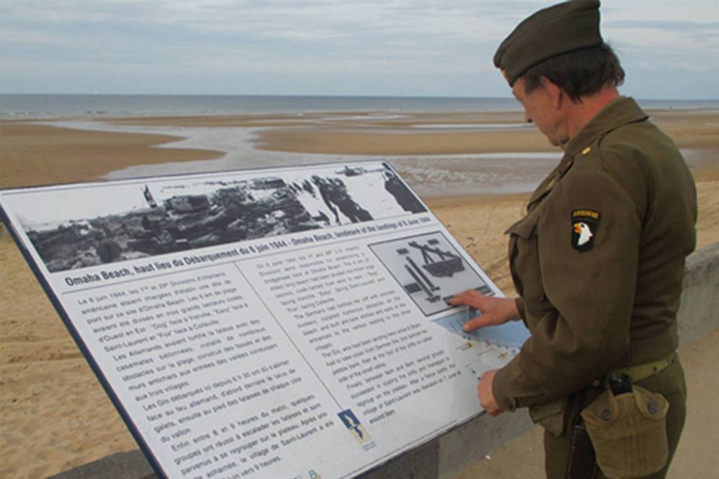 An unidentified World War II reenactor in uniform reading a commemorative sign overlooking the Normandy beach designated Omaha Beach by Allied strategists for the D-Day invasion. Photo submitted by Mac Macdonald.