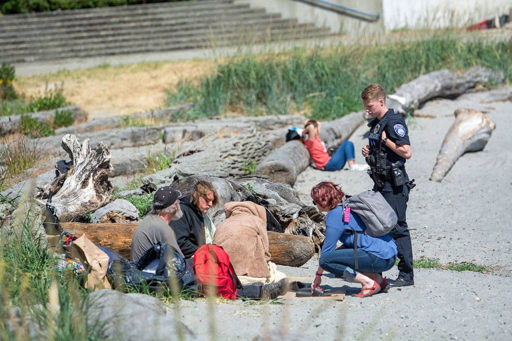 Port Angeles Police Department Officer Jasckson VanDusen and REdisCOVERY Community Change Agent Amy Miller, talk with people resting at Hollywood Beach. (Jesse Major/Peninsula Daily News)