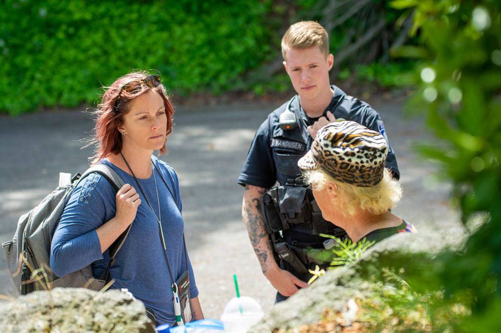 Community Change Agent Amy Miller, of the REdisCOVERY program, and Officer Jackson VanDusen talk with a a homeless veteran at Veterans Memorial Park. (Jesse Major/Peninsula Daily News)
