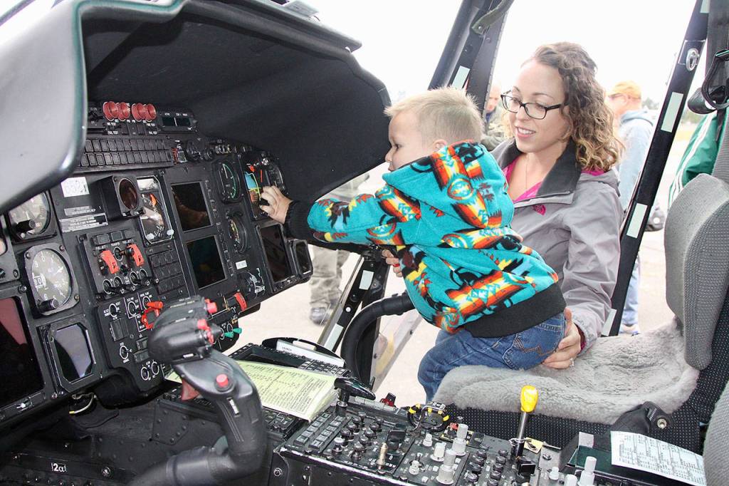 Barron Stangle, 2, of Port Angeles tries his hand at the controls of a Coast Guard helicopter on display at Airport Appreciation Day at Fairchild International Airport on Saturday as his mom, Ariana, watches. This was one of over a dozen displays and attractions at the airport event. (Dave Logan/for Peninsula Daily News)