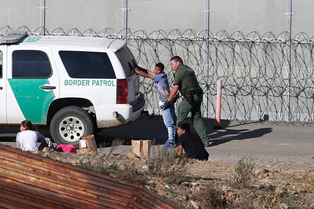 In this Dec. 15, 2018, file photo, Honduran asylum seekers are taken into custody by U.S. Border Patrol agents after the group crossed the U.S. border wall into San Diego, Calif., seen from Tijuana, Mexico. (Moises Castillo/The Associated Press)