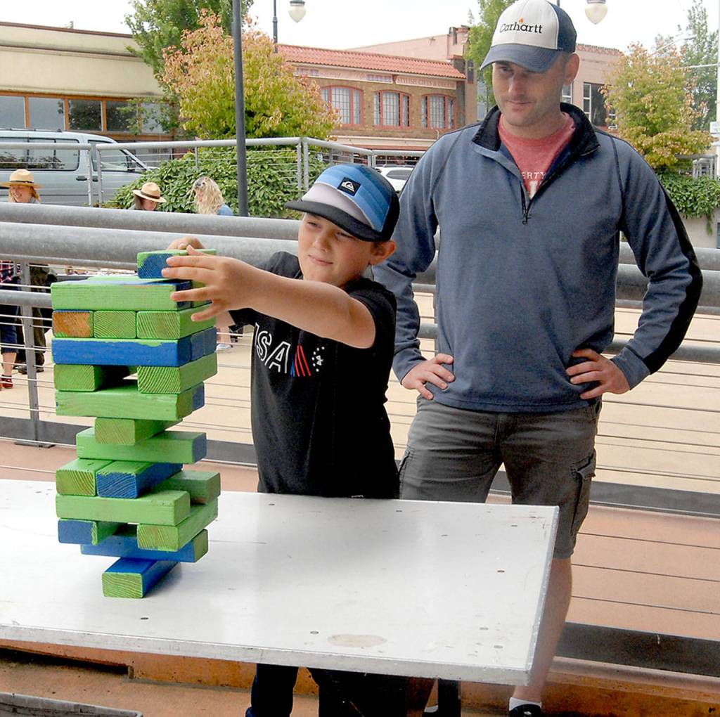 Craig Wilcox of Oak Harbor, right, watches as his son, Cooper Wilcox, 11, places a block in a game of giant Jenga during childrens activities at the pavillion at The Gateway in downtown Port Angeles on Independence Day. (Keith Thorpe/Peninsula Daily News)
