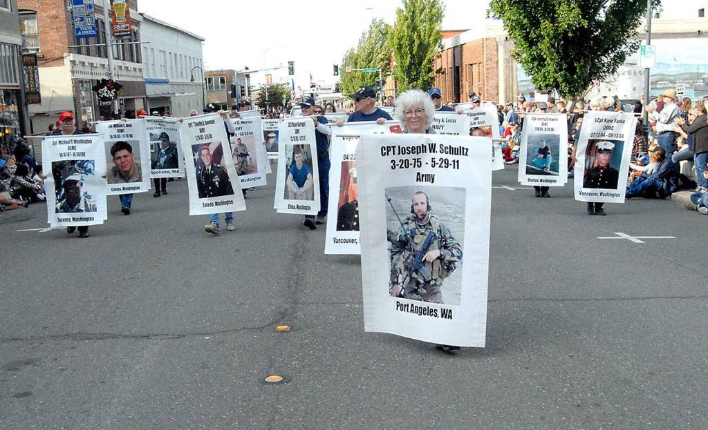 Betsy Schultz of Port Angeles, center, carries a banner with a photo of her fallen son as part of a parade entry honoring Washington military personnel killed in action. (Keith Thorpe/Peninsula Daily News)