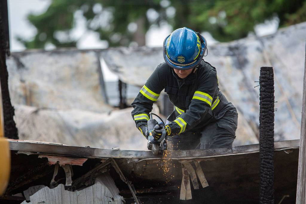 An ATF agent cuts through debris at the scene of a fire in Port Angeles, where the bodies of a mother and three children were found. (Jesse Major/Peninsula Daily News)