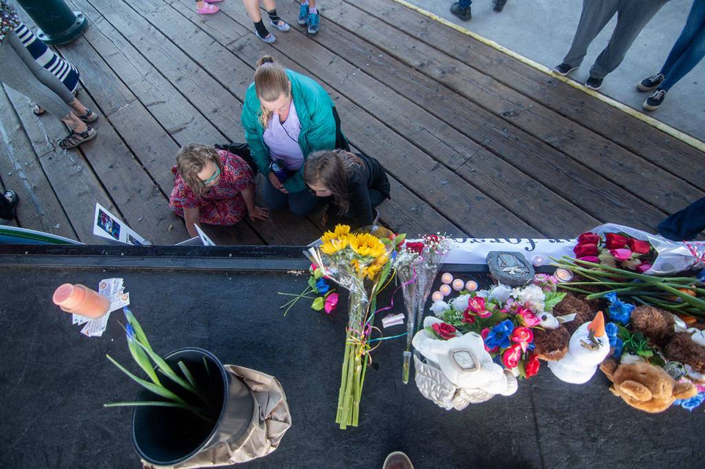 A woman and two children look over photos of Valerie Kambeitz and her children Lilly, Emma and Jayden Kambeitz during a vigil in their honor Monday. (Jesse Major/Peninsula Daily News)