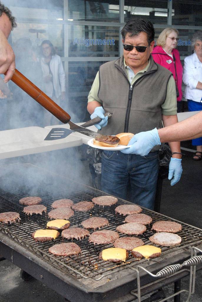 Willie Dueno keeps watch on a grill filled with hamburgers for hungry car show visitors. (Keith Thorpe/Peninsula Daily News)
