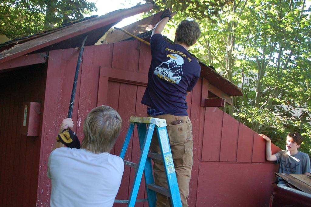 Eagle scout candidate Ian Thill, right, removes a section of the Pioneer Memorial Park storage sheds roof while Dylan Washburn, left, supports a larger section with a prybar. Washburn is an Eagle Scout himself and said that he wanted to lend his experience and support to his friend going through the same process. (Conor Dowley/Olympic Peninsula News Group)