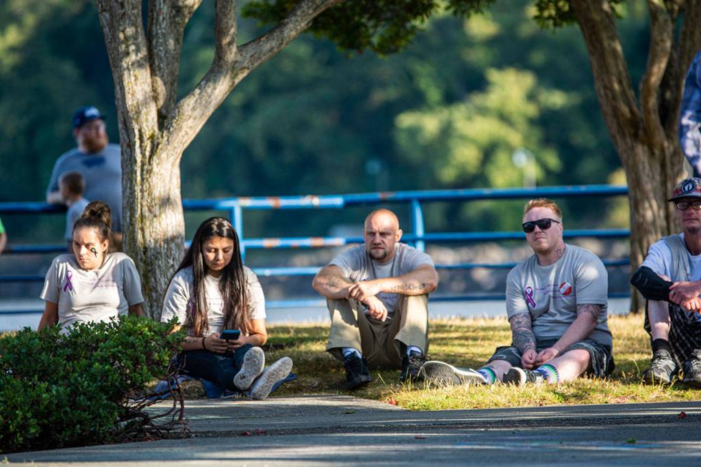 People sit on the grass at City Pier while people speak about recovery Saturday. (Jesse Major/Peninsula Daily News)