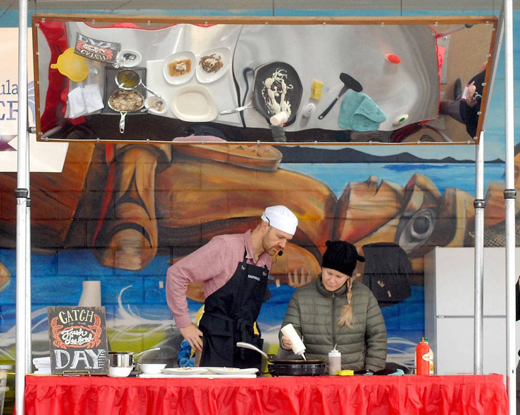 Celebrity cheff Nathan Shields of Saipancakes in Port Angeles, left, gets assistance from audience member Haley Snider of Port Angeles with making decorated pancakes during a cooking demonstration in the pavilion at The Gateway transit center, a venue of the Dungeness Crab and Seafood festival in downtown Port Angeles. (Keith Thorpe/Peninsula Daily News)