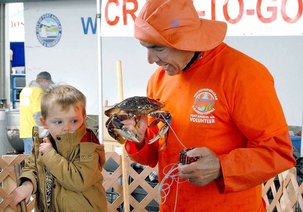 Three-year-old Hayden Fuller of Seabeck is wary as Robert Rohner of Sequim, a member of the North Olympic Peninsula Chapter of Puget Sound Anglers, gives the youngster a close up view of the crab he just caught during Saturdays crab derby at Port Angeles City Pier, a featured event of the Dungeness Crab and Seafood Festival. (Keith Thorpe/Peninsula Daily News)