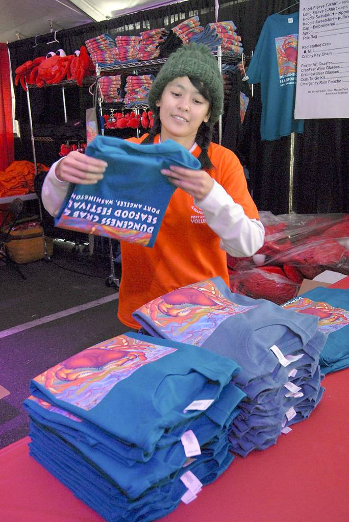 Volunteer Tien Vo of Port Angeles stacks festival T-shirts at a merchandise table Friday in the Dungeness Crab and Seafood Festival main tent in Port Angeles. (Keith Thorpe/Peninsula Daily News)