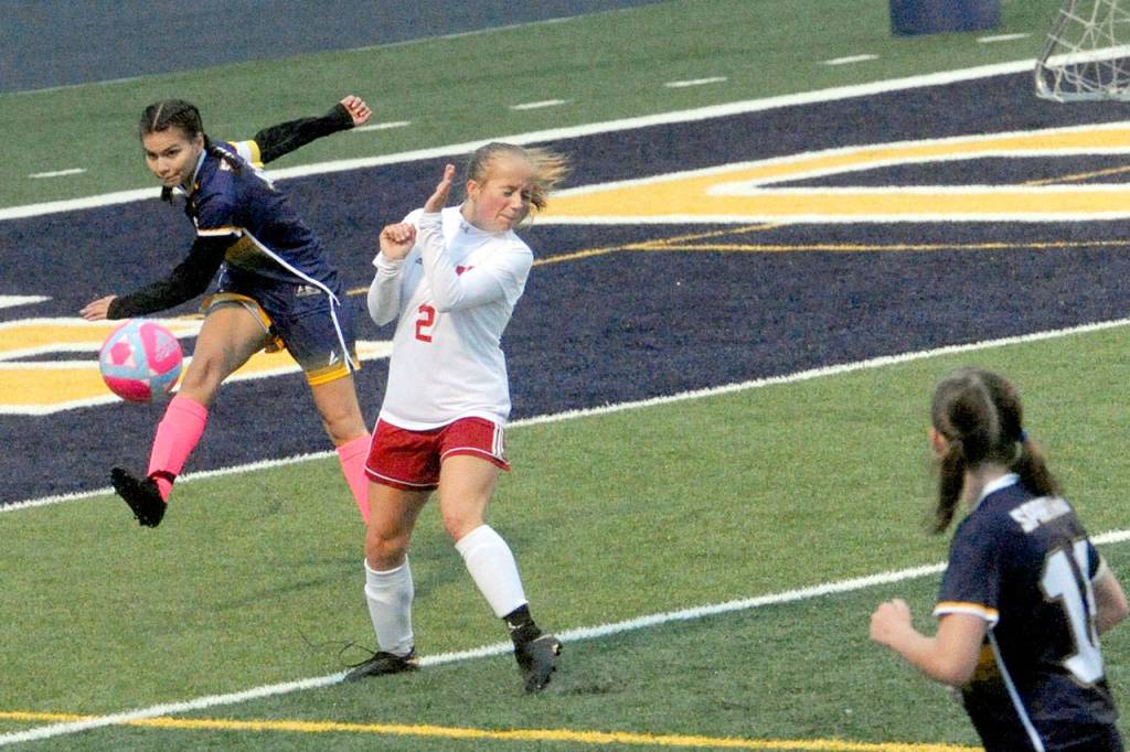 Spartan Candida-Rose Sandoval (left) kicks past Hoquiams Sadie Carlyle (2) during a rain storm at Spartan Stadium where the Grizzlies defeated Forks 2-0 on a wet and windy Spartan Stadium turf. Forks wore pink socks and used a pink and white soccer ball during this cancer awareness night. (Lonnie Archibald/for Peninsula Daily News)