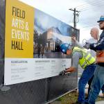 Chris Fidler, executive director of the Field Arts and Events Hall, center, gets assistance from Don Frostad, left, and Clayton Frohman of general contractor M.A. Mortenson Company as they peel back the protective cover from a project sign at the future site of the performing arts center at Front and Oak streets on the Port Angeles waterfront. (Keith Thorpe/Peninsula Daily News file)