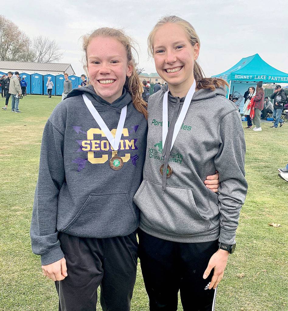 Sequims Riley Pyeatt, left, and Port Angeles Lauren Larson, celebrate their sixth-place and fifth-place medals, respectively, at the state 2A Girls Cross-Country Championship held in Pasco on Saturday.