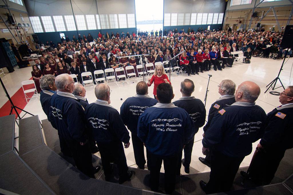 Linda Muldowney directs the Olympic Peninsula Mens Chorus during the Veterans Day ceremony at U.S. Coast Guard Air Station/Sector Field Office Port Angeles on Monday. (Jesse Major/Peninsula Daily News)