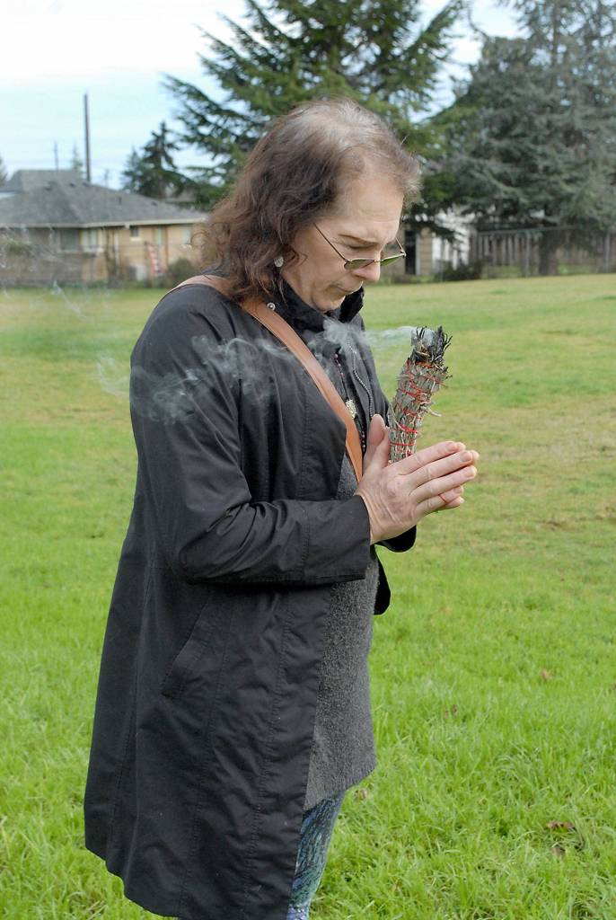 Jasmine Hunt, who lives near Lions Park in Port Angeles, holds a bundle of burning sage on Friday as she marks the one-year annniversary of the felling of a controversial sequoia tree that once towered over the neighborhood. (Keith Thorpe/Peninsula Daily News)