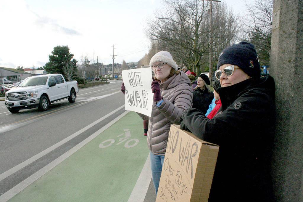 Elaine Sullivan, left, and Melanee Knudsen, both from Port Townsend, join about 100 people Thursday in the No War protest at the intersection of East Sims Way and Kearney Street in Port Townsend. Both said they have been protesting U.S. military actions since the Vietnam War. Unfortunately, these senseless wars weve been protesting for 50 years, Knudsen said. None of these wars have gotten us anywhere. (Brian McLean/Peninsula Daily News)