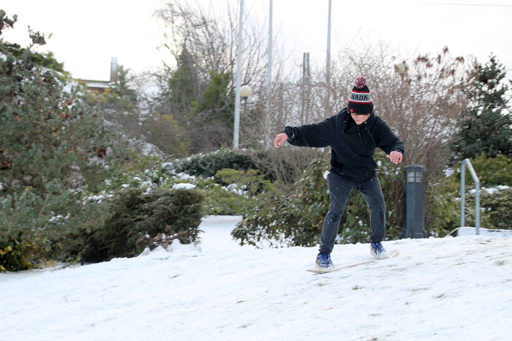 Lucas Chase, 14, rides his makeshift snowboard down the hill at the 9/11 Memorial Waterfront Park on Tuesday. Chase took a skateboard, removed the wheels, covered the bottom in gorilla tape and applied wax in hopes to make it down the hill. (Maureen Heaster/Peninsula Daily News)