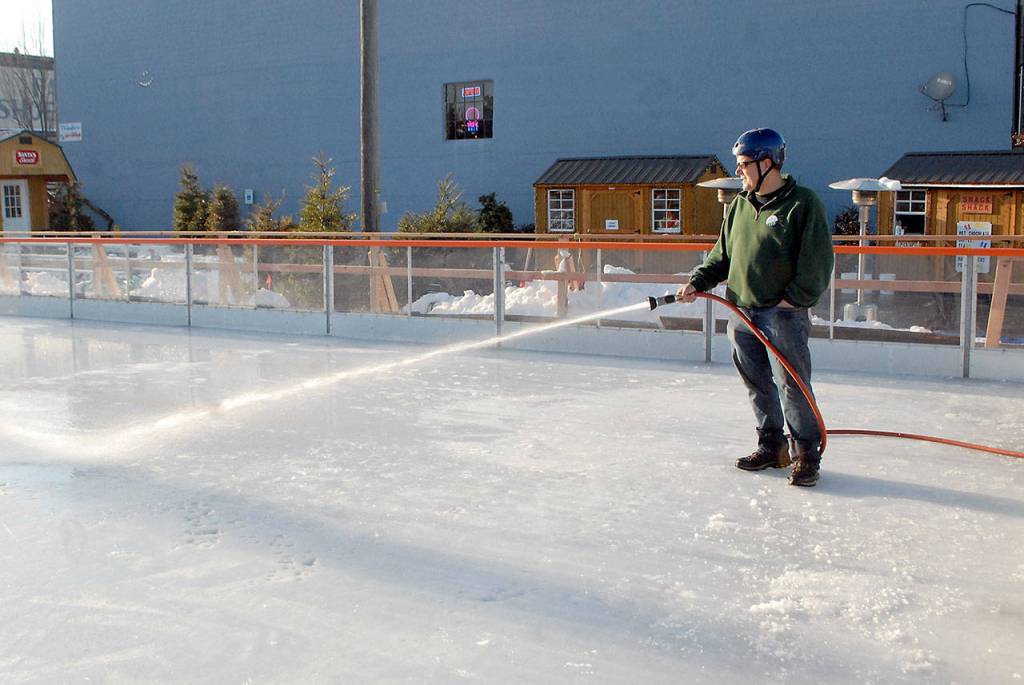 Marc Abshire, executive director of the Port Angeles Regional Chamber of Commerce, sprays water on the now-open-air ice skating rink at the Port Angeles Ice Village on Thursday afternoon after the rink was cleared of the collapsed tent. (Keith Thorpe/Peninsula Daily News)