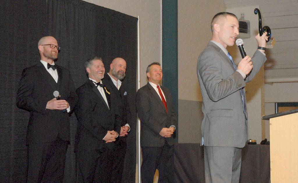 Rian Anderson of Black Ball Ferry holds up his companys Chamber of Commerce Legacy Award on Saturday as masters of ceremony, from left, Josh Jones, Tim Tucker, Terry Ward and Jim Haguewood look on. (Keith Thorpe/Peninsula Daily News)