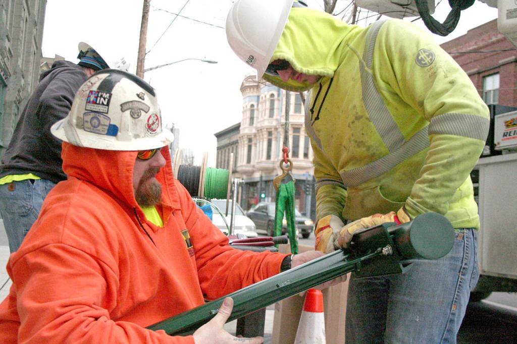 FB Titan Powerline crew member Michael Lake, left, works with Jimmy Holmes to secure the electrical wiring inside one of the new street lights on Water Street in downtown Port Townsend on Monday, Jan. 27, 2020. The crew, which included foreman Drew Plato, back left, will continue its work today between Tyler and Taylor streets. (Brian McLean/Peninsula Daily News)
