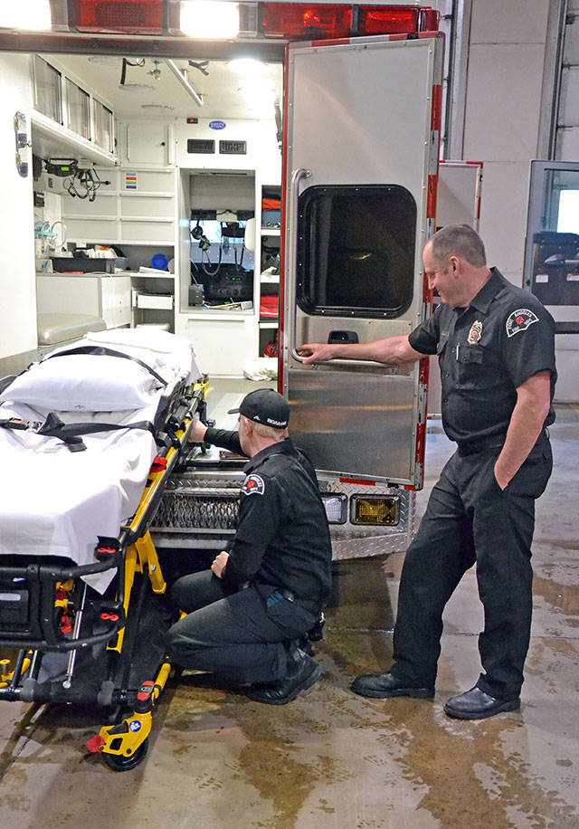 Paramedic Mike Ingraham, left, checks the functionality of a new ambulance stretcher while senior EMT Todd German assists. (Laura A. Foster/Peninsula Daily News)