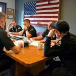 The Port Angeles Fire Department B Shift sits down together for a morning briefing on local coronavirus protocol. From left, clockwise, are paramedics Doug Eaton and Tyler Wildeman, Capt. Kelly Ziegler, paramedic Tyler Gage, EMT Todd German and paramedic Mike Ingraham. Out of frame is Lt. Jeremy Church. (Laura Foster/Peninsula Daily News)