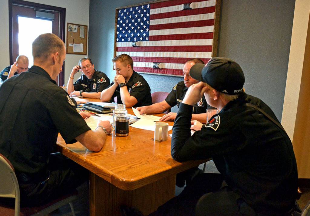 The Port Angeles Fire Department B Shift sits down together for a morning briefing on local coronavirus protocol. From left, clockwise, are paramedics Doug Eaton and Tyler Wildeman, Capt. Kelly Ziegler, paramedic Tyler Gage, EMT Todd German and paramedic Mike Ingraham. Out of frame is Lt. Jeremy Church. (Laura Foster/Peninsula Daily News)