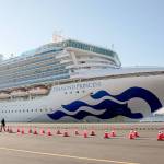 A reporter walks near the quarantined Diamond Princess cruise ship in Yokohama near Tokyo on Tuesday, Feb. 11, 2020. Japans Health Minister Katsunobu Kato said the government was considering testing everyone remaining on board and crew on the Diamond Princess, which would require them to remain aboard until results were available. (Jae C. Hong/The Associated Press)