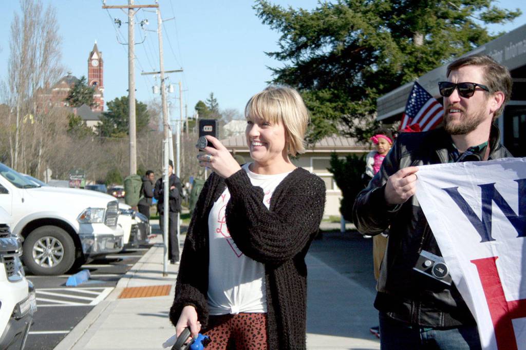 Kate Krusely, left, captures the moment her husband, U.S. Navy Lt. Julian Krusely, steps off a bus Tuesday. Meanwhile, Brian Wright of Los Angeles holds a banner that reads Welcome Home along with his wife, Jennifer (not pictured). (Brian McLean/Peninsula Daily News)