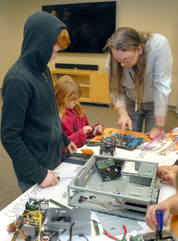 North Olympic Library System information technology specialist Bob Allen assists Lincoln Anton, 11, and Sydney Anton, 9, with computer disassembly. (Keith Thorpe/Peninsula Daily News)