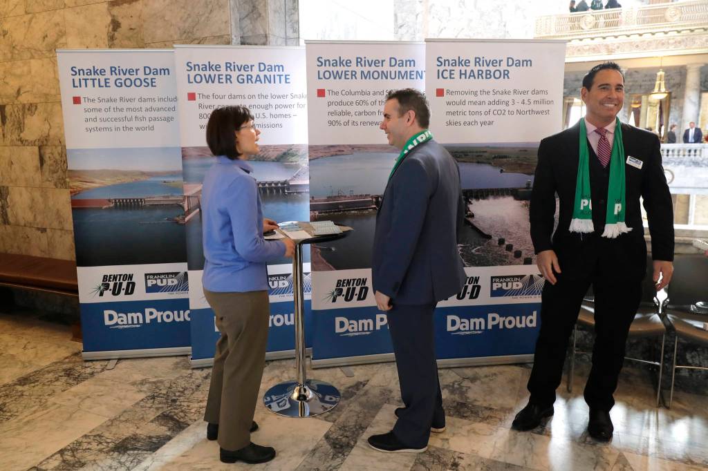 In this Feb. 12, 2020, photo, Mike Gonzalez, right, senior manager of public affairs at the Franklin Public Utility District, stands next to informational signs promoting dams on the Snake River during a lobby day at the Capitol in Olympia, Wash. A federal report released Friday, Feb. 28, rejected the idea of removing four hydroelectric dams on a major Pacific Northwest river in a last-ditch effort to save threatened and endangered salmon. The report says breaching the dams would destabilize the power grid, increase greenhouse emissions and raise the risk of power outages. (AP Photo/Ted S. Warren)