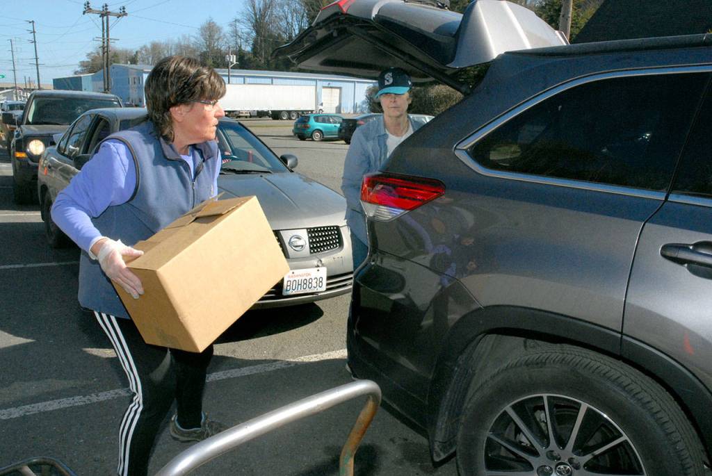 Fran Howell, left, lift a pre-packaged box of food as Connie Panike, prepares to load it into a car on Friday outside the Port Angeles Food Bank. In response to the outbreak of the novel coronavirus, the food bank is not allowing patrons to come into close contact with food bank workers. (Keith Thorpe/Peninsula Daily News)