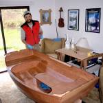 Northwest Maritime Center instructor Joel Arrington stands in his living room with a completed test build of the Portage Pram boat kit that his students will be constructing in the online course starting on April 20. (Kate Philbrick)