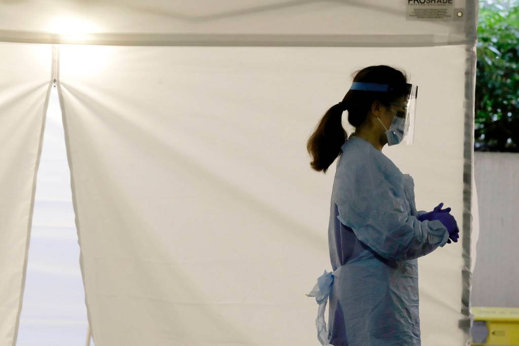 A nurse at a drive-up coronavirus testing station set up by the University of Washington Medical Center wears a face shield and other protective gear in this March 13 file photo as she waits by a tent in Seattle. Experts and health officials who are trying to plan a response to the coronavirus outbreak are missing a critical piece of information – the number of health care workers who have tested positive for the disease. (Ted S. Warren/The Associated Press)