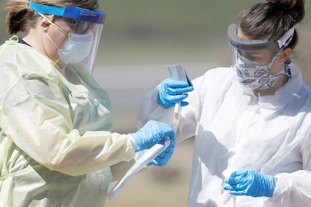 Medical technicians handle a vial containing a nasal swab at a drive-thru testing site in Wheat Ridge, Colo., in this March 31 file photo. Home testing for coronavirus may sound like a good idea, but as of this week, U.S. regulators say its still too risky. (David Zalubowski/The Associated Press)