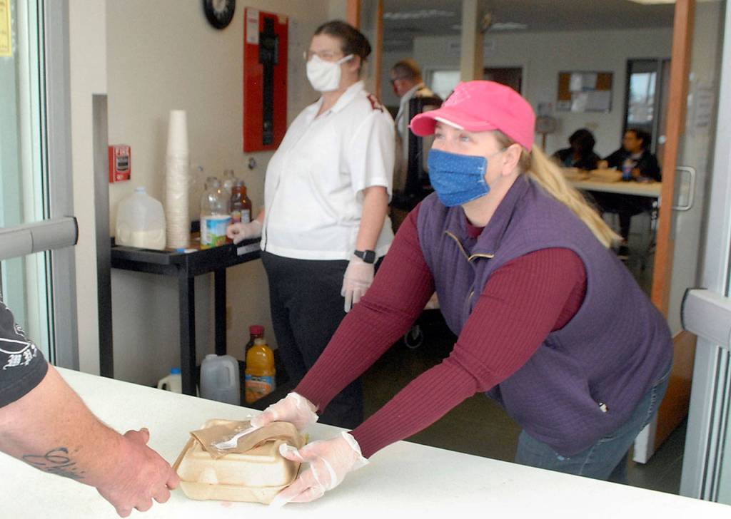 Volunteer Stacy Eastman of Port Angeles, right, passes out a hot meal at the front door of the Salvation Armys Port Angeles kitchen as Major Barbara Wehnau waits to pour beverages on Friday. (Keith Thorpe/Peninsula Daily News)