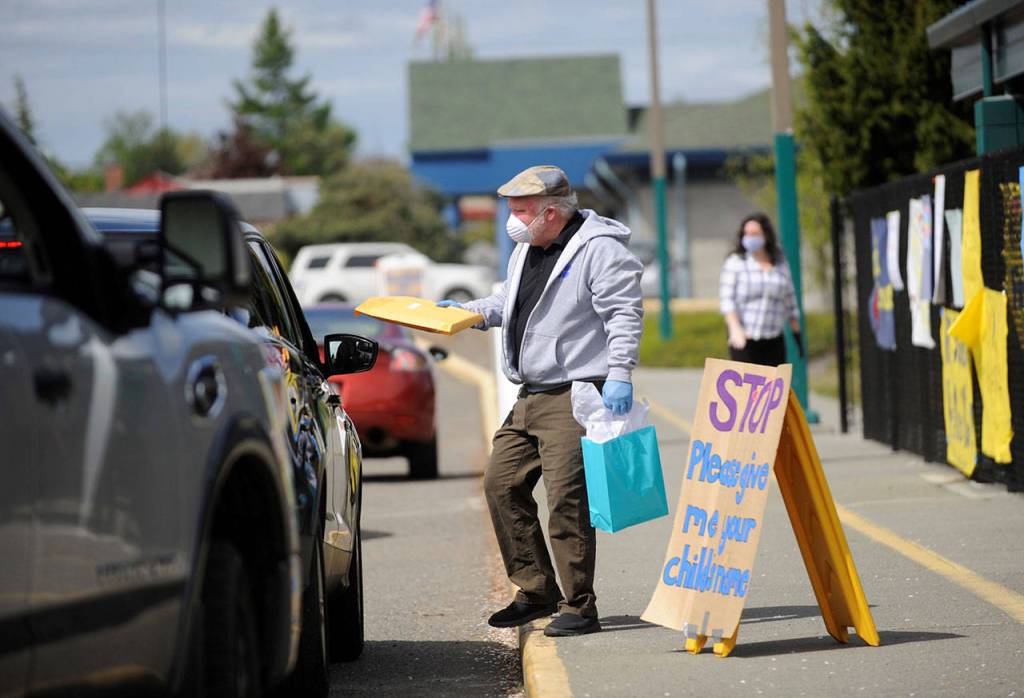 Patrick Caron, a fourth-grade teacher at Helen Haller Elementary School, hands out a homework packet to a Haller student in April. (Michael Dashiell/Olympic Peninsula News Group file)