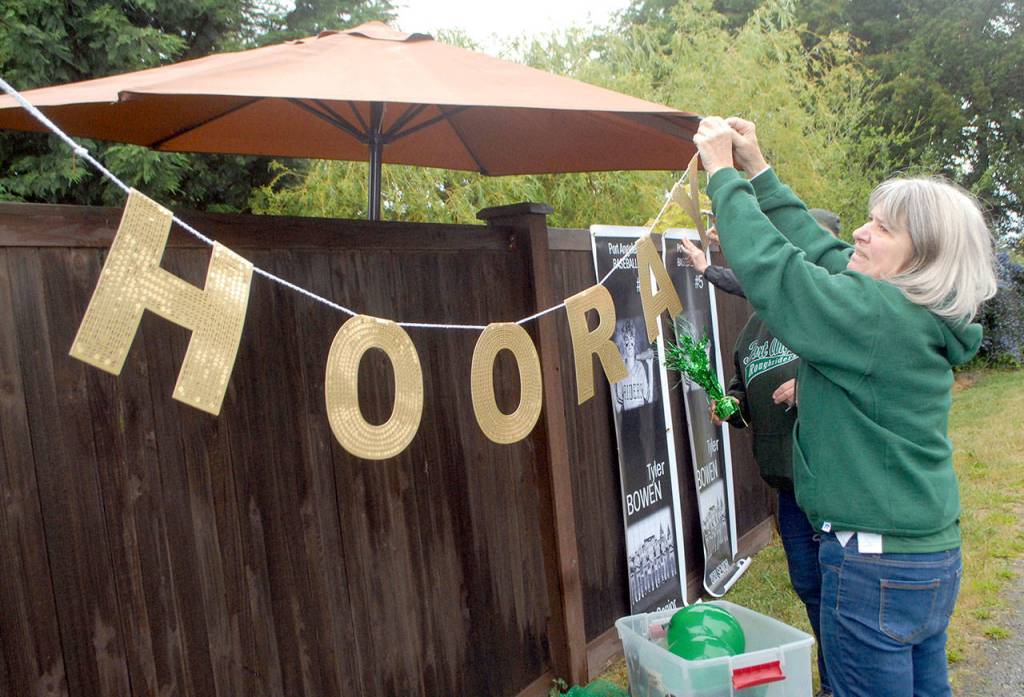 Sudi McLaughlin, grandmother of graduating senior Tyler Bowen, hangs a message for members of the Port Angeles High School Class of 2020 in front of a house along the route of a motorcade of graduates on Friday in Port Angeles. (Keith Thorpe/Peninsula Daily News)